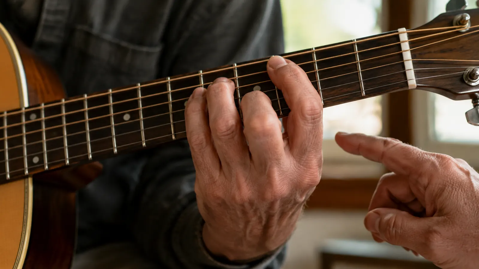 Close view of a left hand fretting a chord shape on an acoustic guitar during a lesson